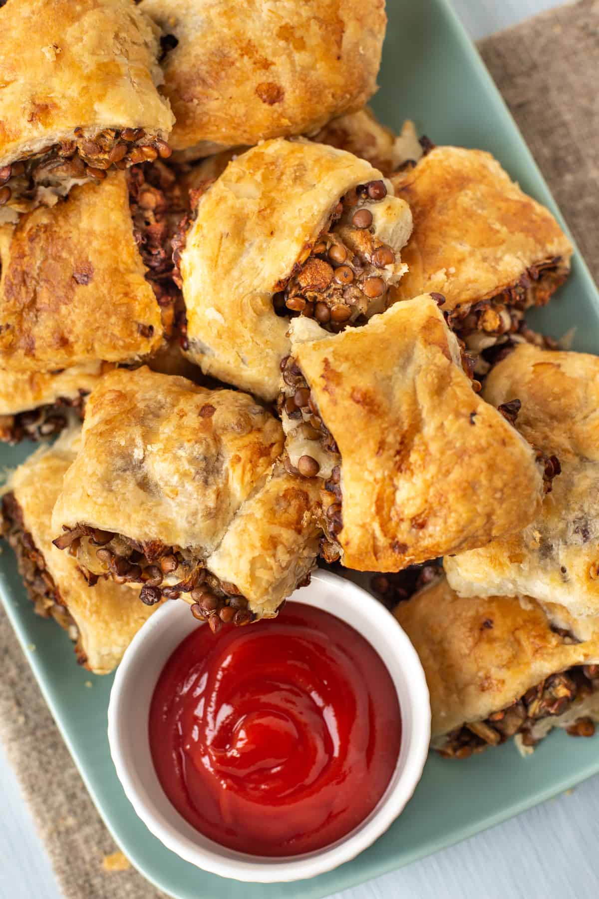 A plateful of vegetarian sausage rolls piled up with a pot of ketchup.