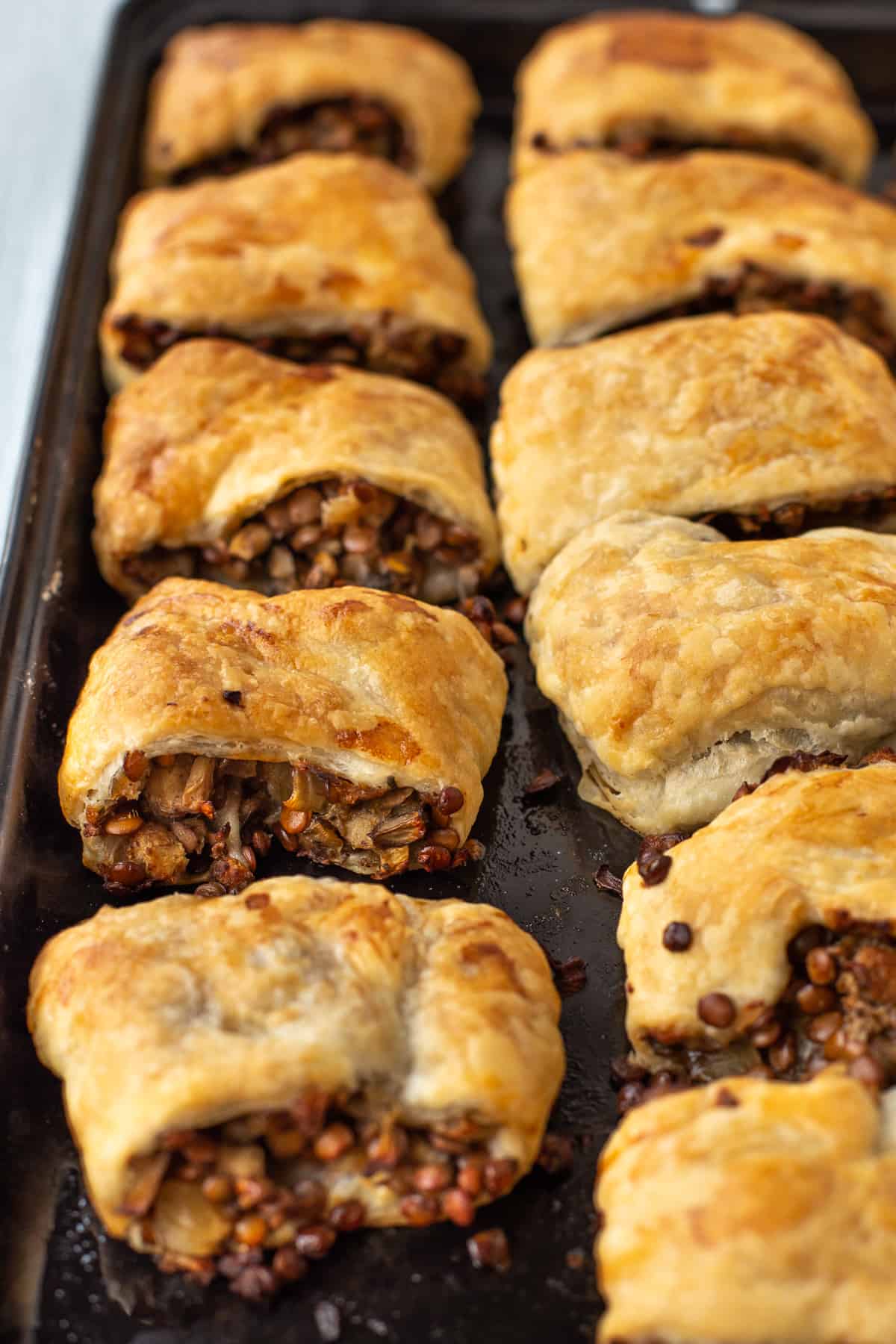 A baking tray full of crispy vegetarian lentil sausage rolls.