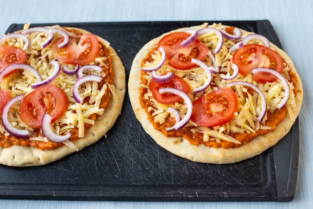 Uncooked lentil pizzas topped with tomatoes and red onion on a cutting board.