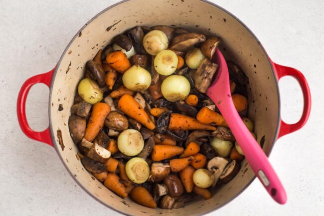 Uncooked baby onions, baby carrots and mushrooms in a large Le Creuset casserole dish.