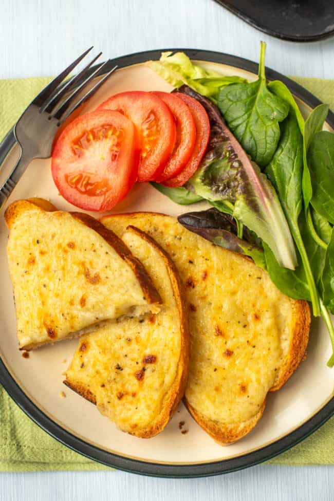 Two slices of cheese on toast on a plate with tomatoes and salad.