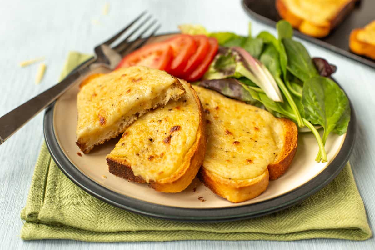Two slices of cheesy Welsh rarebit on a place with tomatoes and lettuce.