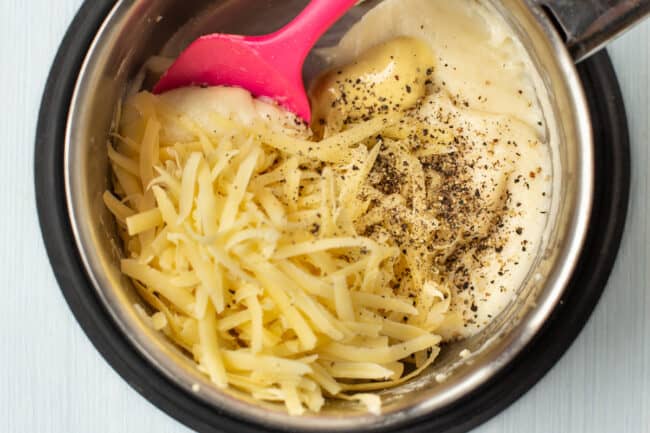 Grated cheese and black pepper being added to a white sauce in a saucepan.