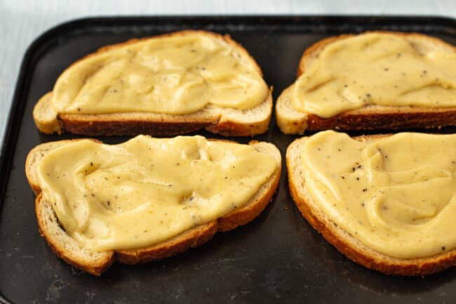 Welsh rarebit sauce spread over some slices of bread on a baking tray.