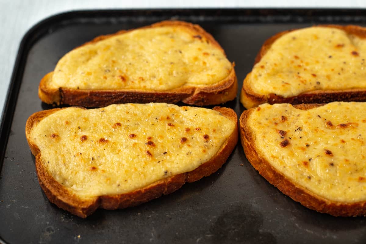 Slices of crispy Welsh rarebit on a baking tray.