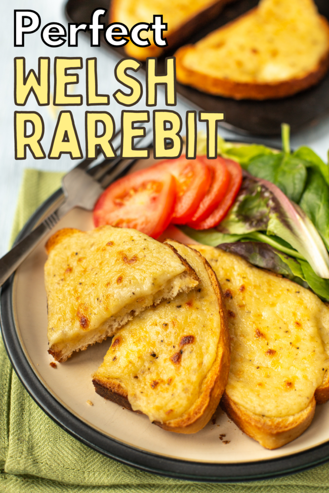 Two slices of cheesy Welsh rarebit on a plate with tomatoes and lettuce.
