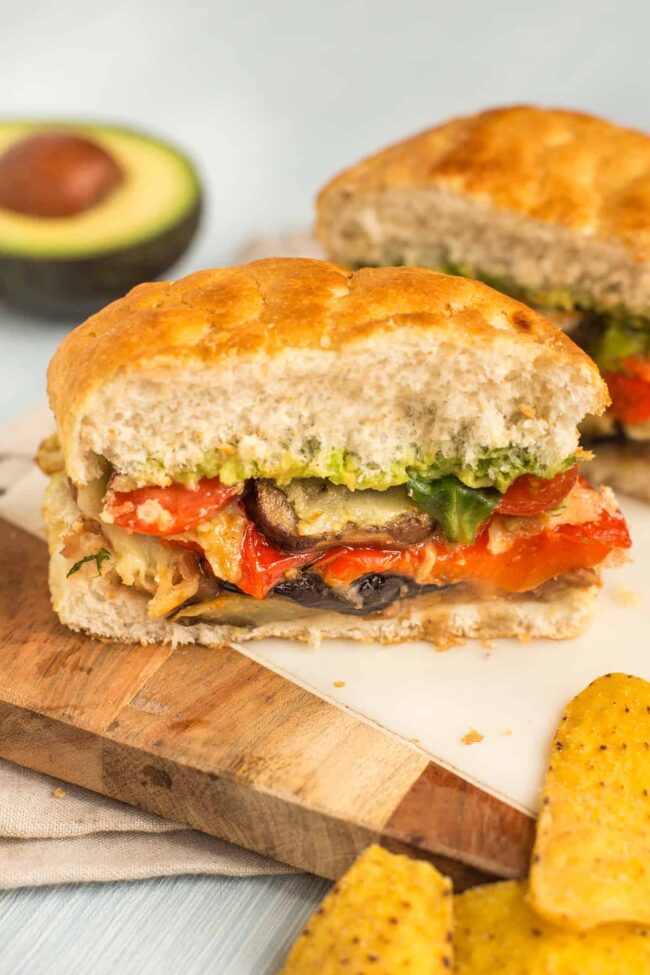 A vegetarian sandwich cut in half, filled with cheesy roasted veg and mashed avocado.