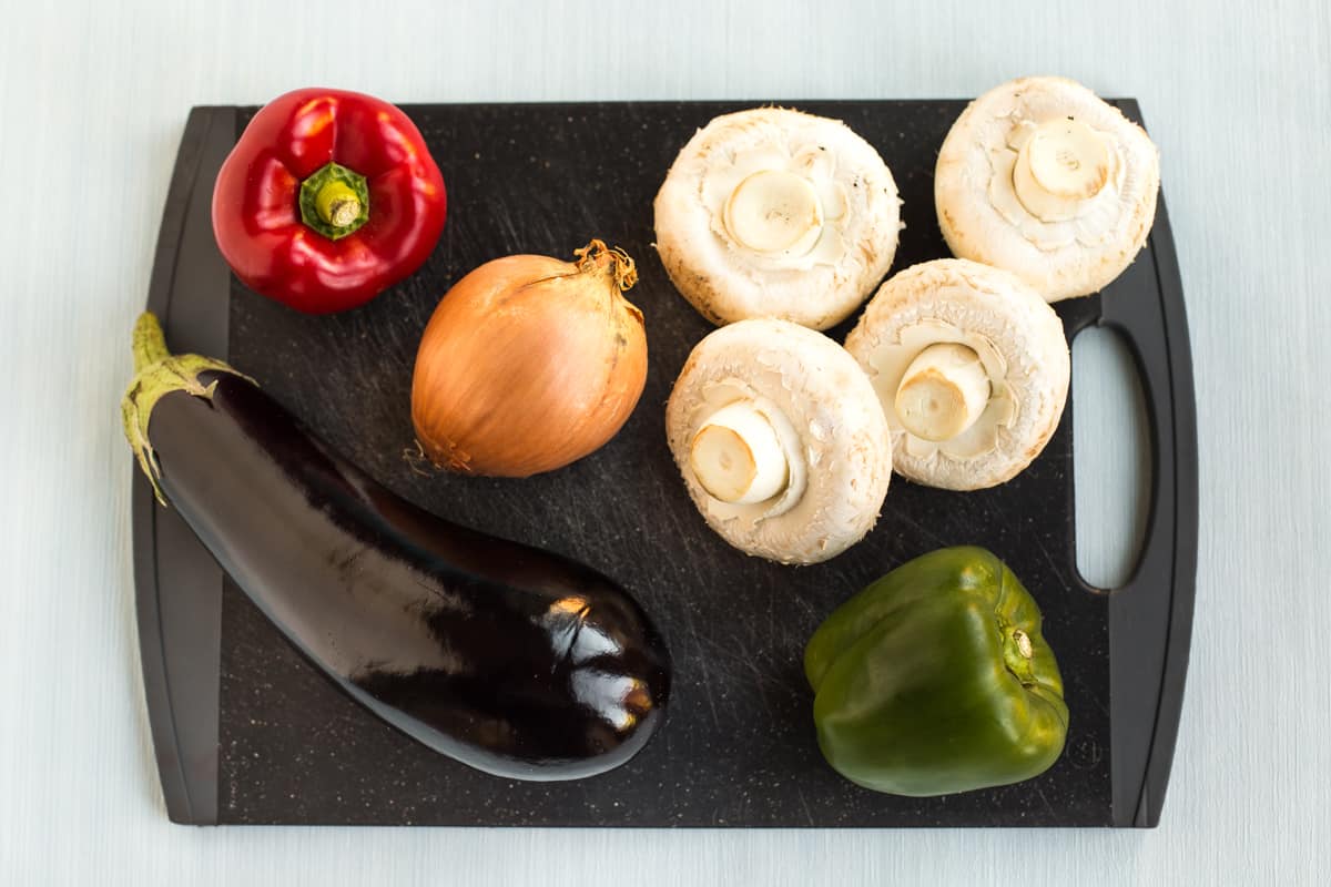 A selection of Mediterranean vegetables on a black chopping board.