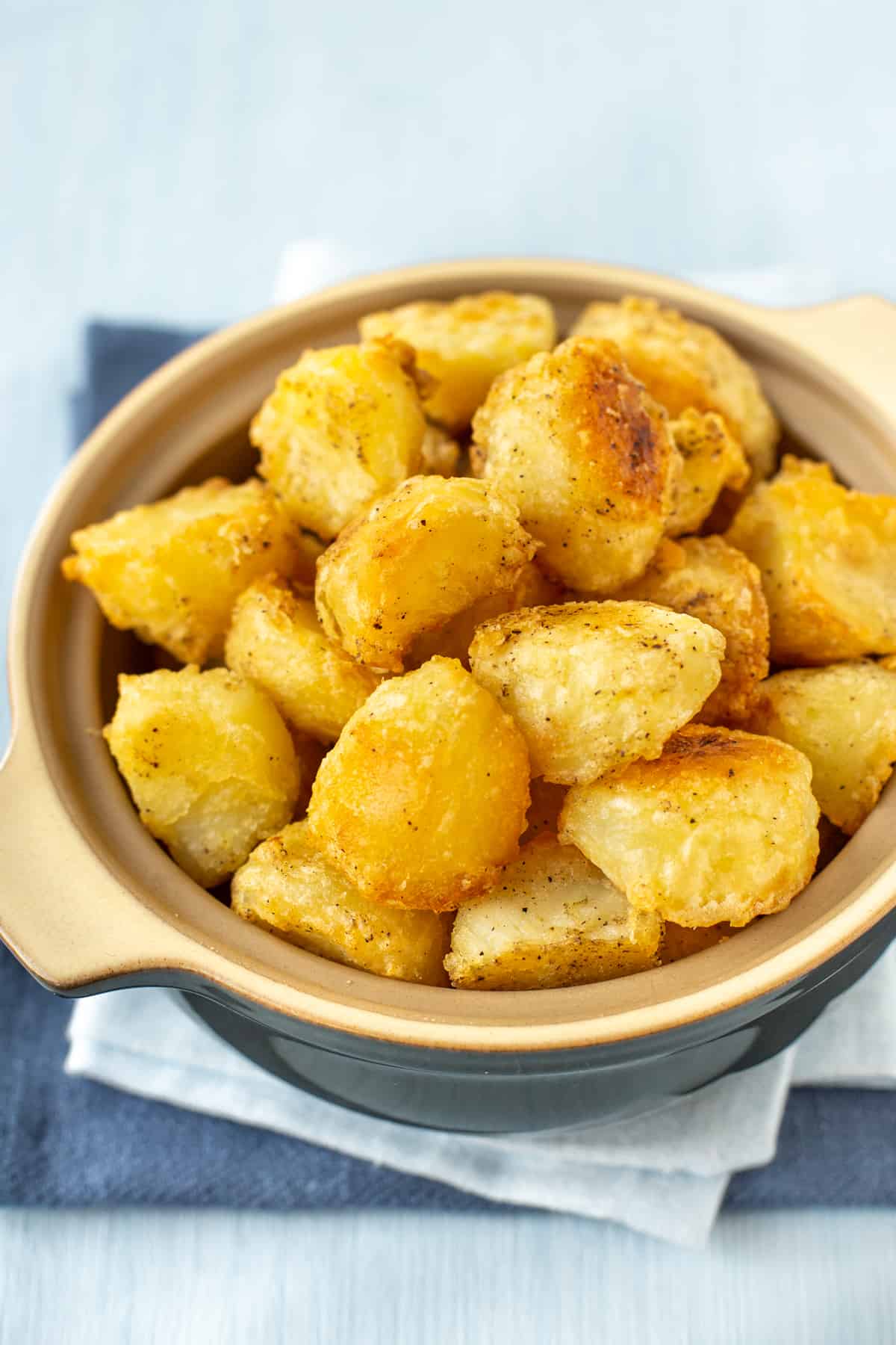 A serving bowl piled high with crispy golden roast potatoes.
