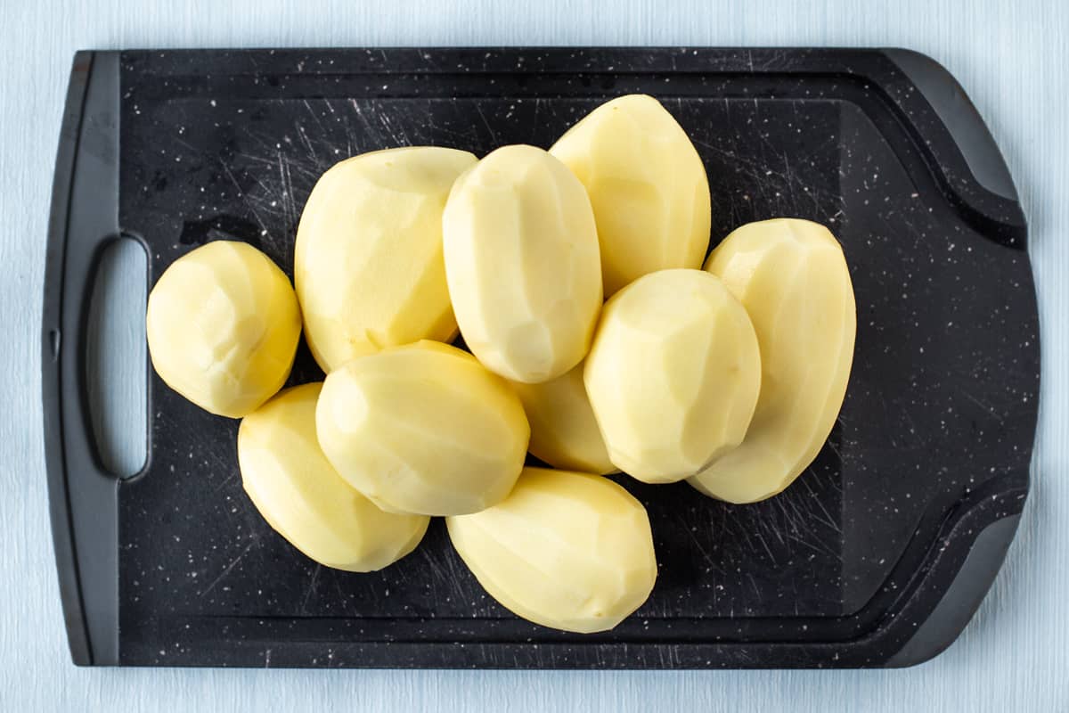 A pile of peeled Maris Piper potatoes on a chopping board.