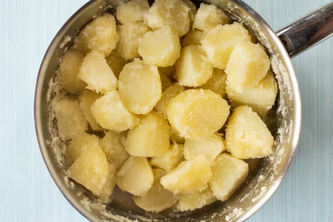 Fluffed up boiled potatoes in a large saucepan, ready for roasting.