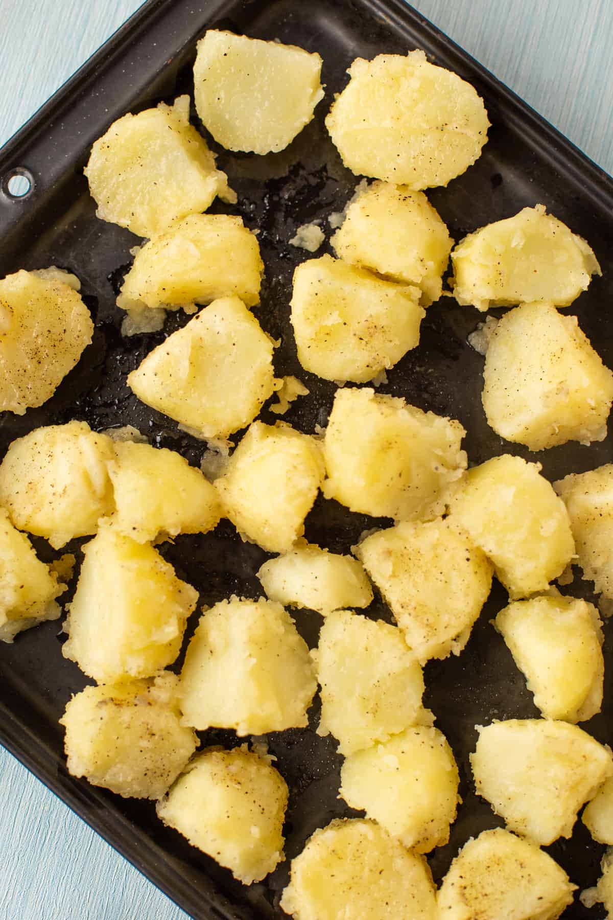 Fluffy boiled potatoes spread out on a baking tray ready to roast.