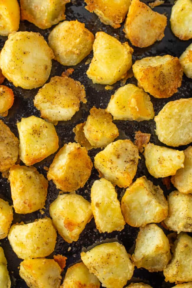 A close up showing a baking tray covered with crispy roast potatoes.