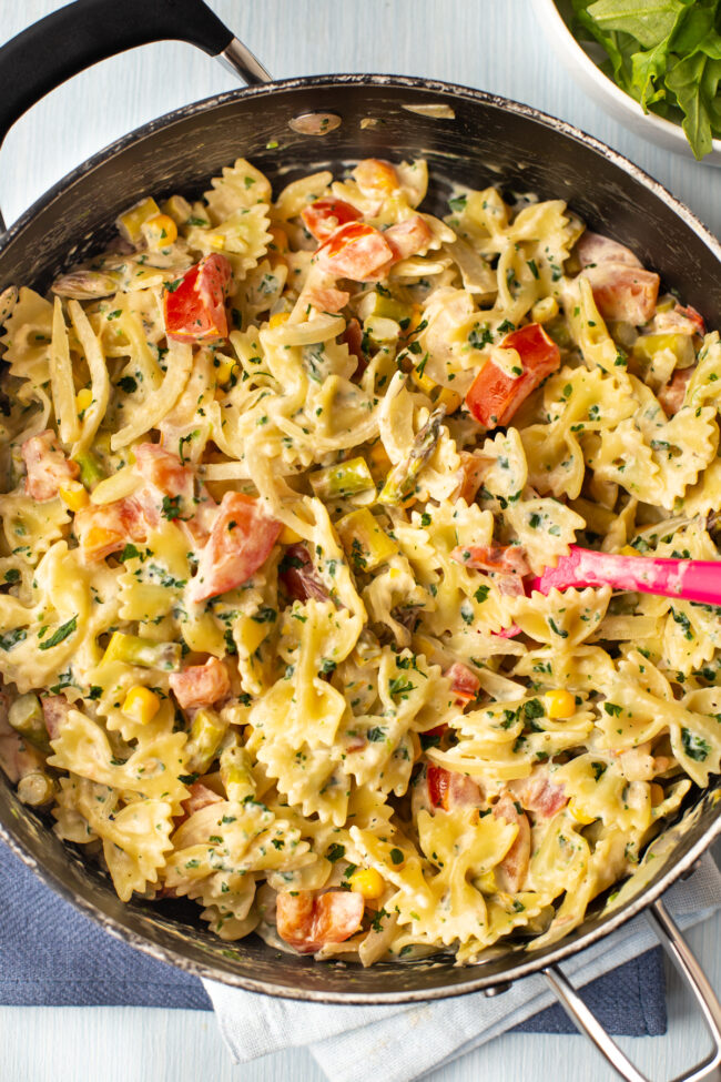 Creamy pasta primavera in a frying pan, with lots of vegetables.