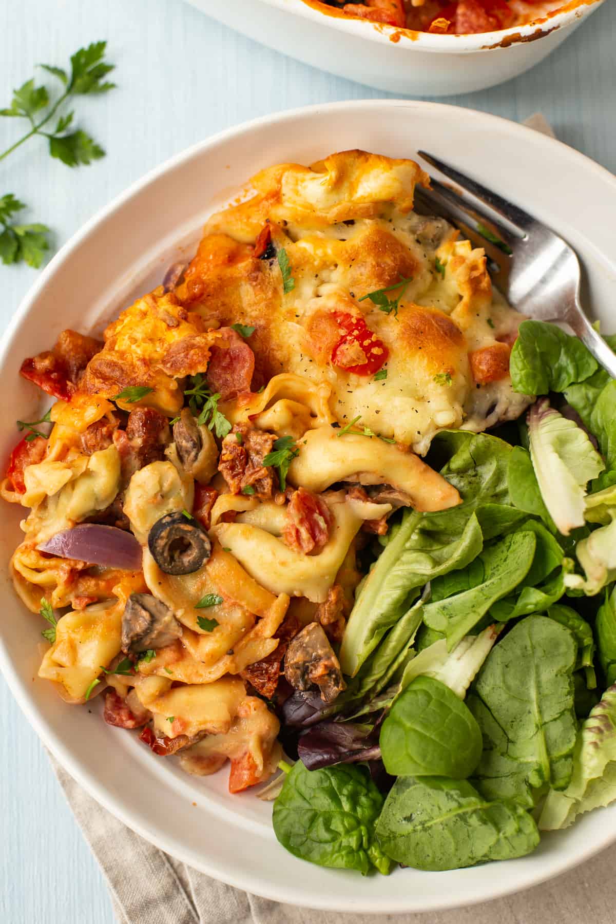A portion of creamy tortellini bake in a bowl with green salad.
