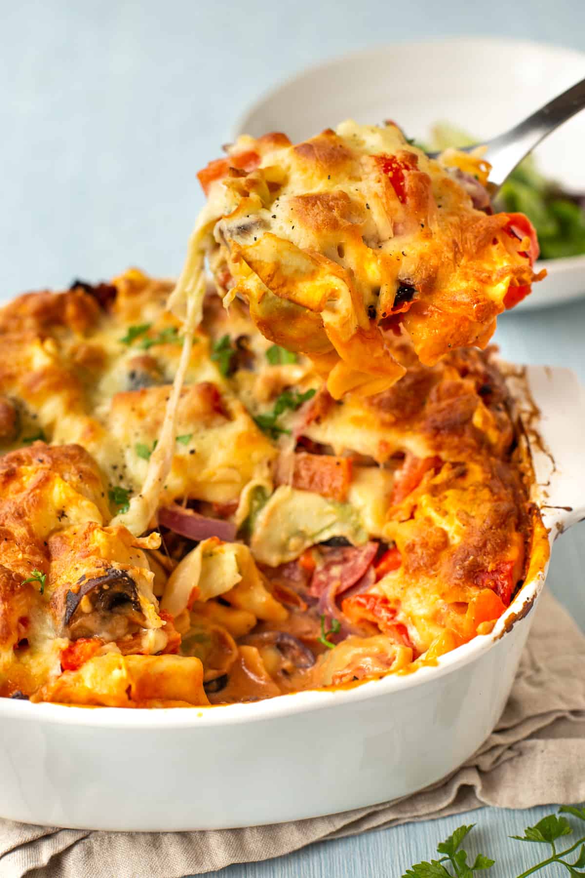 A gooey cheesy scoop of pasta bake being scooped from a dish.