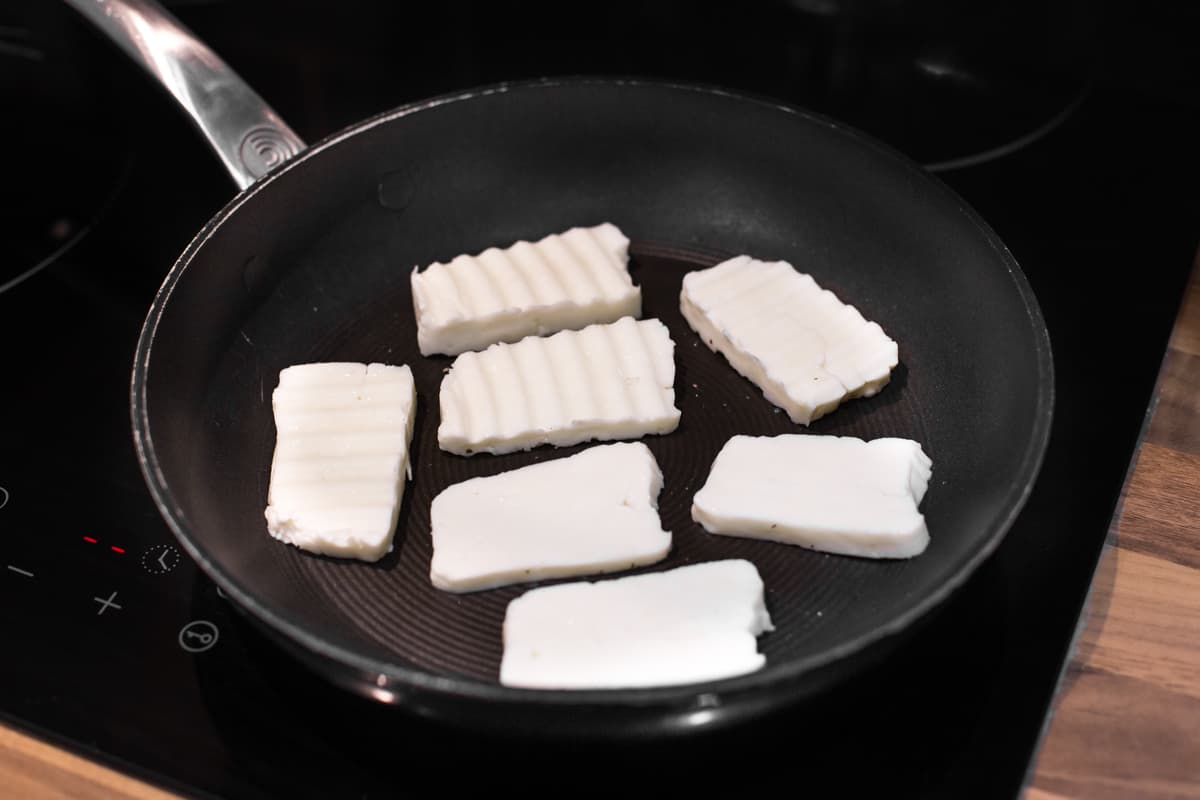 Slices of uncooked halloumi in a frying pan.