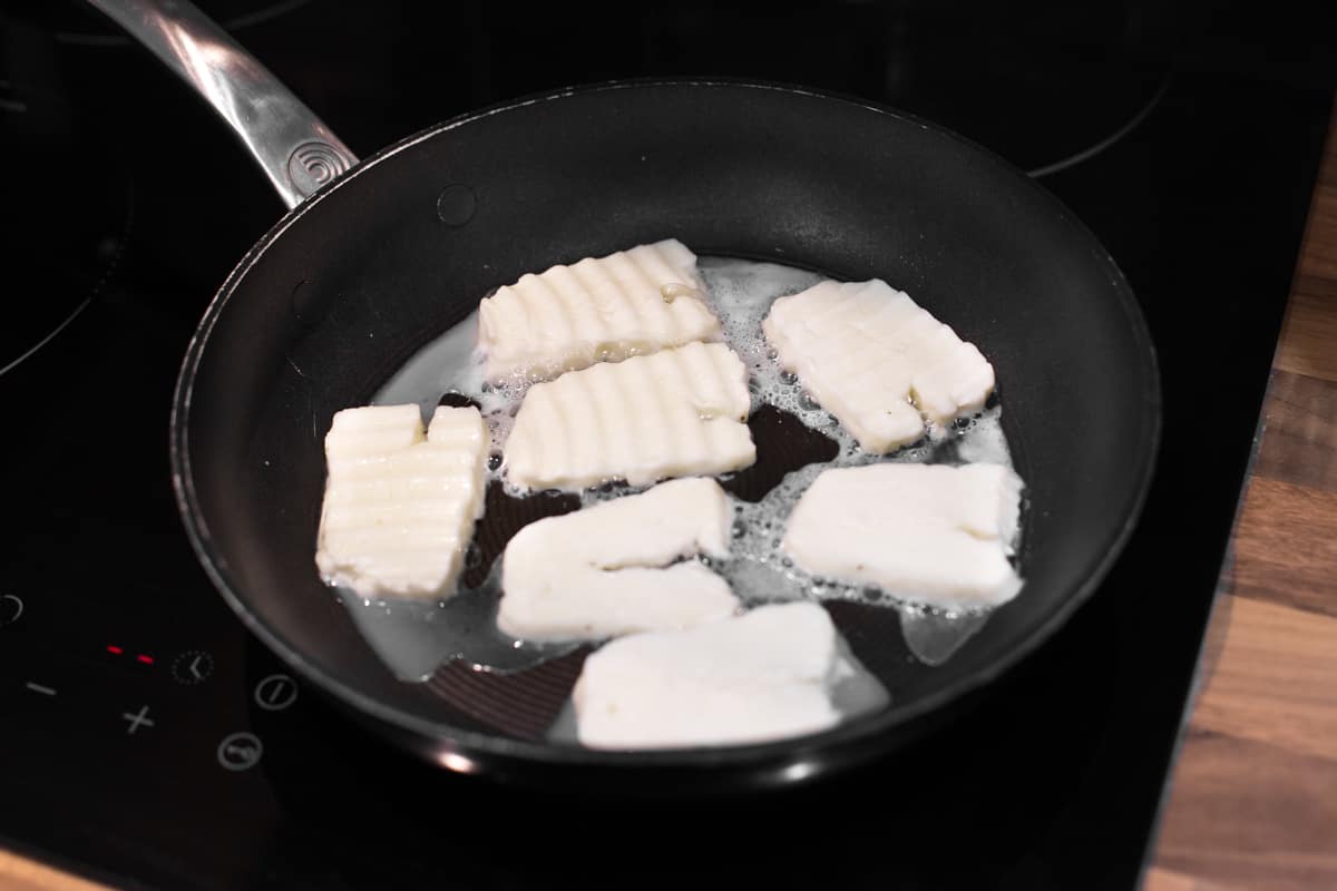Liquid being released by halloumi cheese as it cooks in a frying pan.