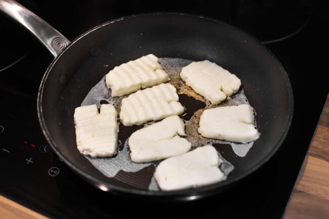 Halloumi cheese beginning to crisp up in a frying pan.