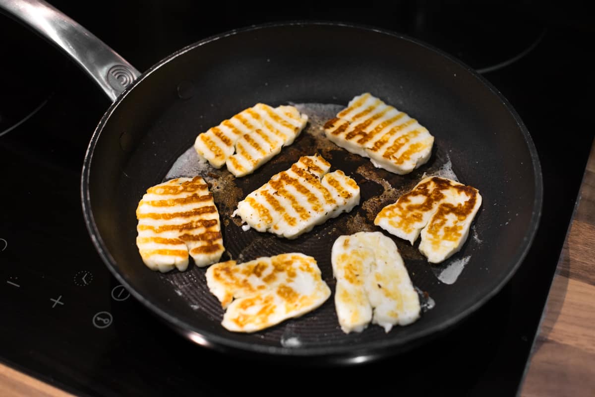 Crispy slices of halloumi cheese in a frying pan.