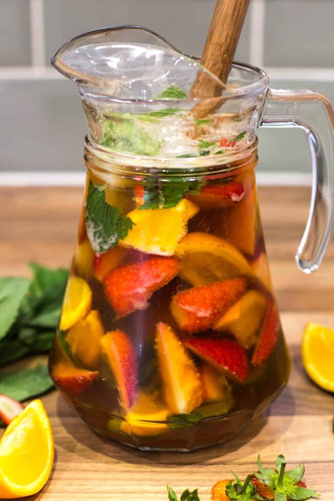 A large jug of Pimm's filled with oranges, strawberries and cucumber.