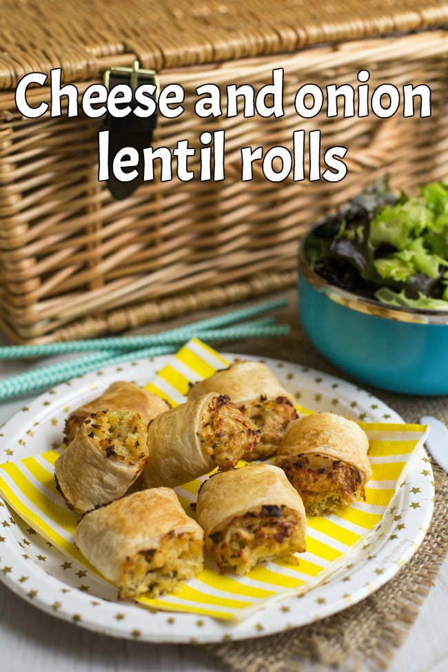 A few cheesy lentil rolls on a paper plate in front of a picnic basket.