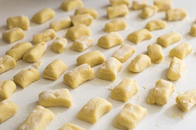 Uncooked homemade gnocchi dumplings spread out on a worktop.
