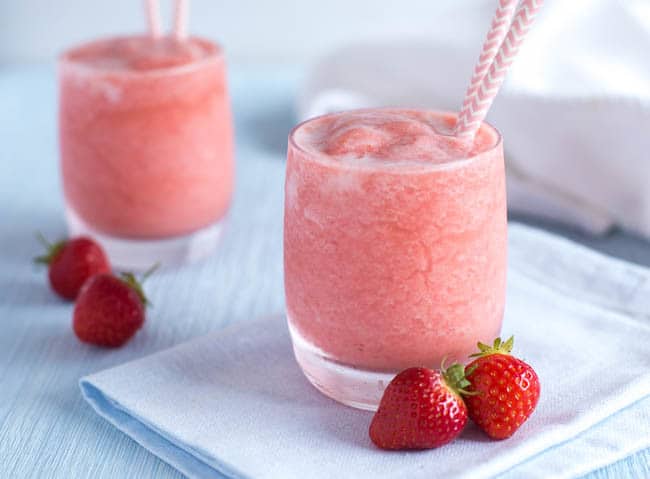 Bright pink cocktails in glasses with straws and fresh strawberries.