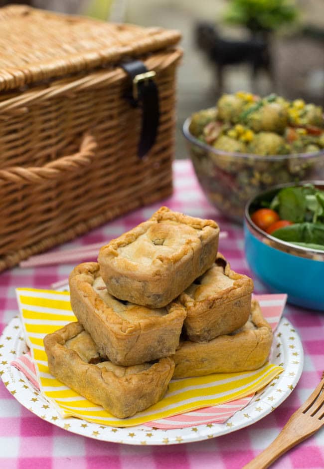 A stack of mini picnic pies on a paper plate on a picnic rug.