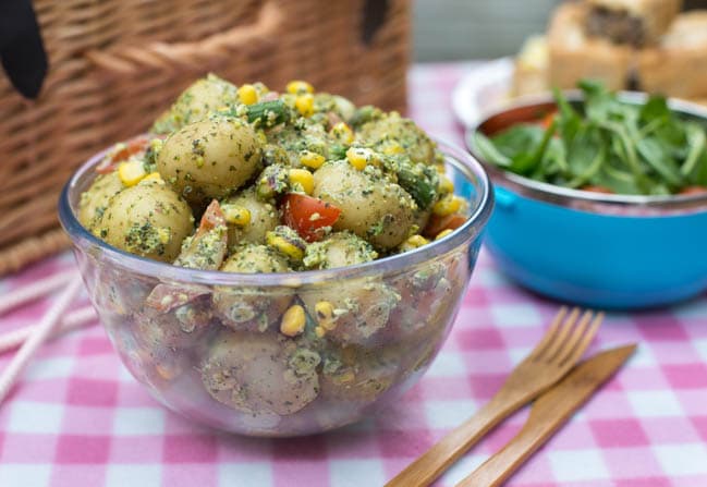 A bowlful of pesto potato salad on a picnic mat in front of a wicker basket.