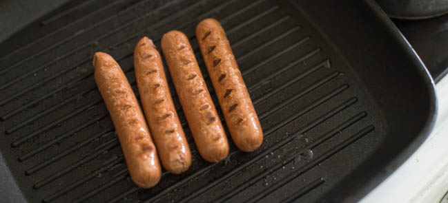 Vegetarian hot dog sausages cooking on a griddle.