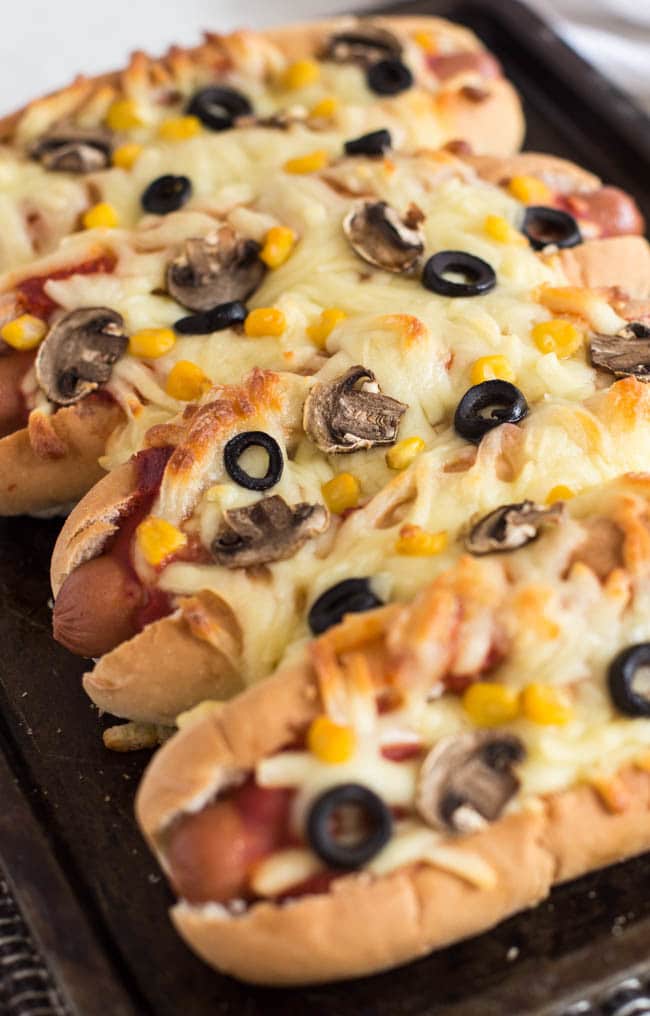 A row of cheesy pizza-topped hot dogs on a baking tray.