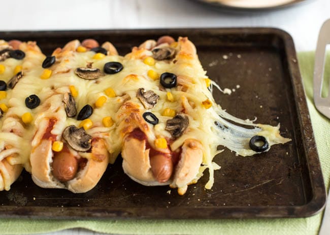 Cheesy hot dogs on a baking tray topped with pizza toppings.