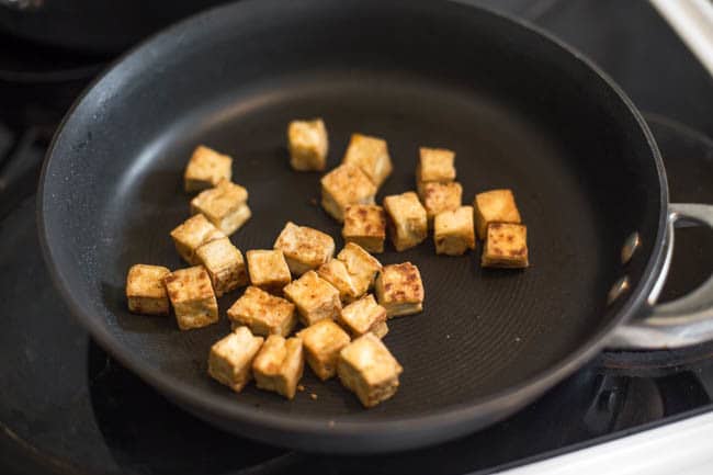 Crispy cubes of tofu cooking in a frying pan.