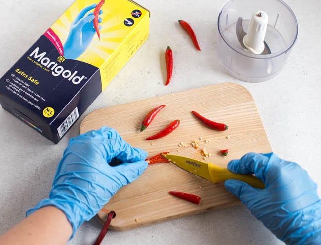 Gloved hands chopping small red birdseye chillies.