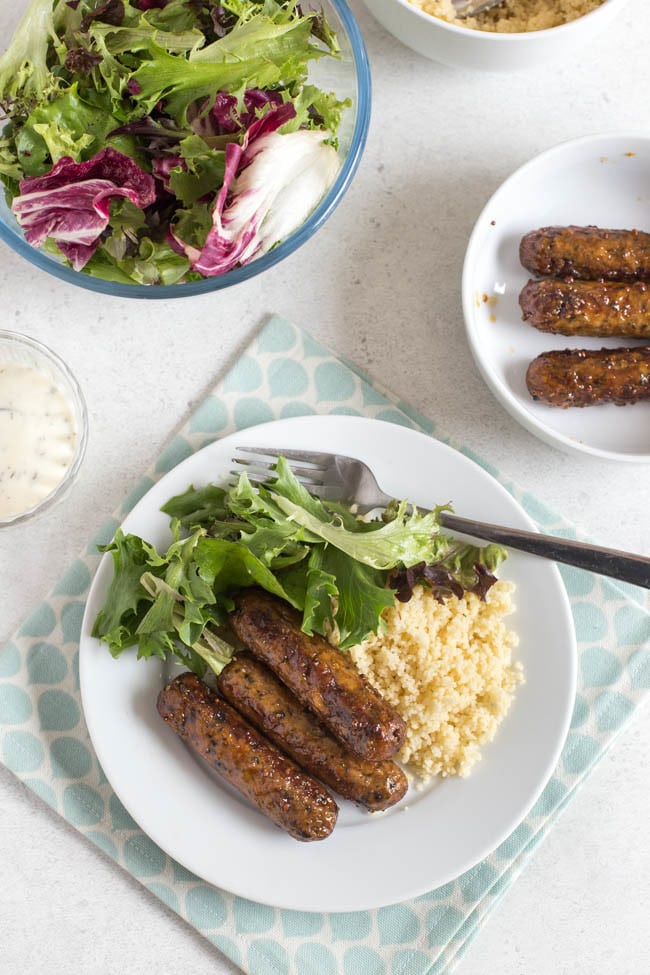 Aerial shot of a plate of sticky glazed sausages with couscous and salad.