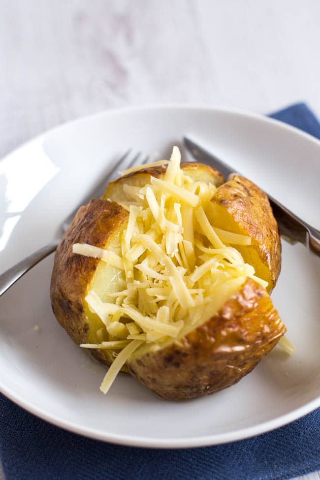 Close up photo of a baked potato stuffed with grated cheese.