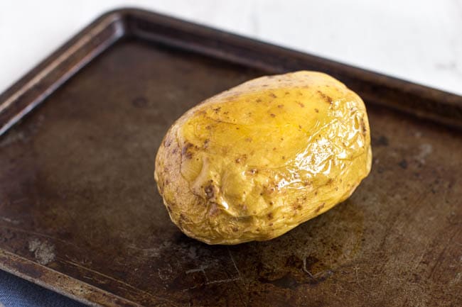 A baked potato rubbed with oil on a baking tray.