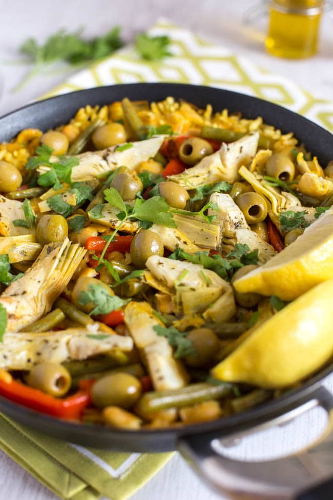 A pan of vegetable paella with olives and artichokes.