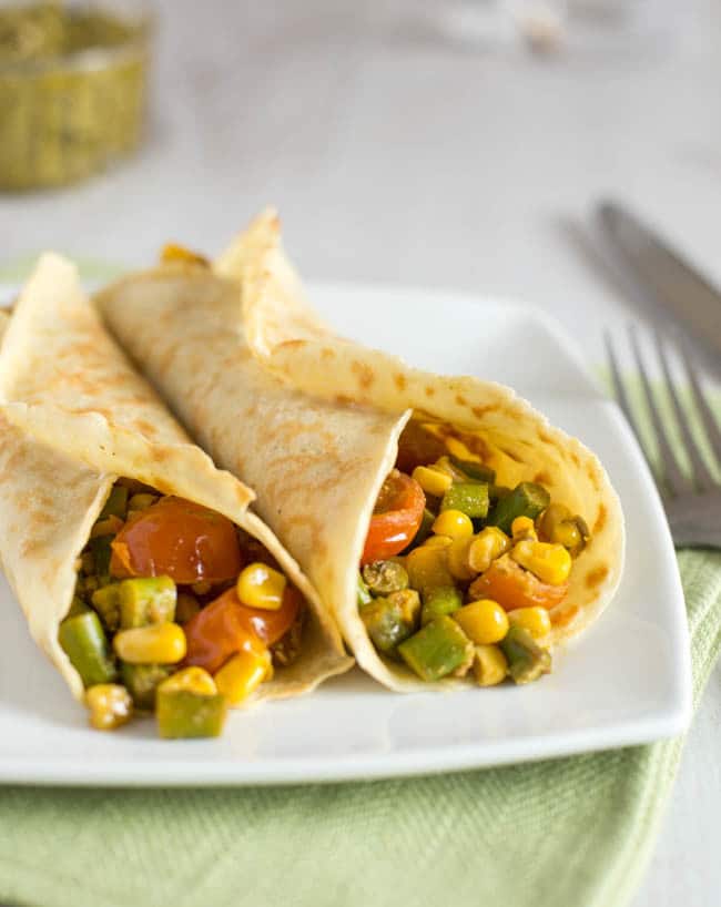 Two savoury pancakes on a plate, rolled up with a vegetable filling.
