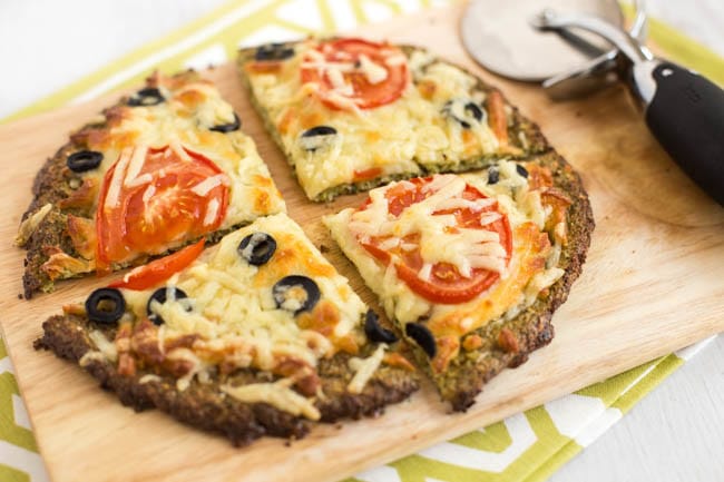 A low-carb broccoli crust pizza topped with tomato slices and black olives.