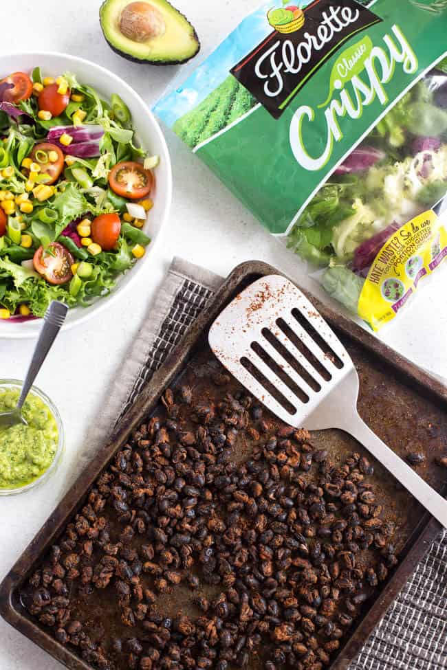 Roasted black beans on a baking tray surrounded by taco salad ingredients.