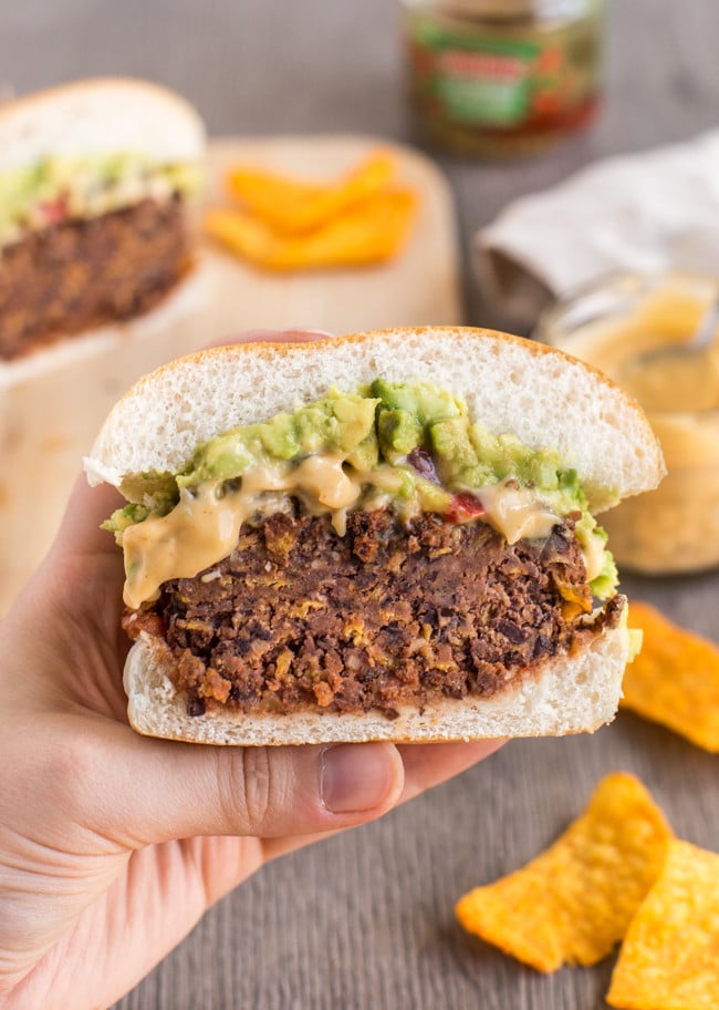 Half a black bean burger topped with guacamole being help up in a hand.