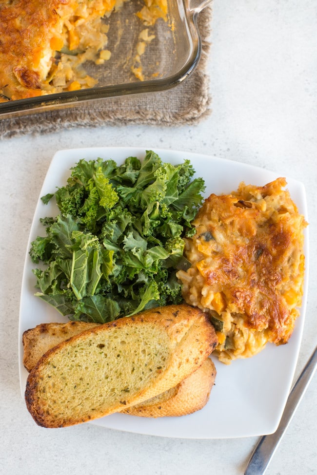 Portion of very veggie lentil bake on a plate with garlic bread and crispy kale.