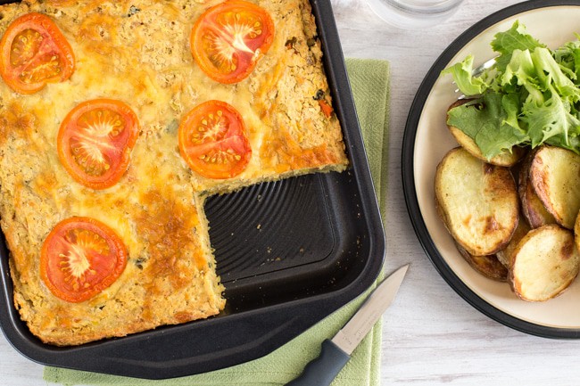 Cheesy lentil slice in a baking dish with a piece removed.