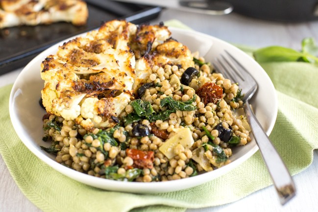 Mediterranean couscous with artichokes and sun-dried tomatoes - served with tasty roasted cauliflower steaks. Vegetarian, vegan, full of flavour!