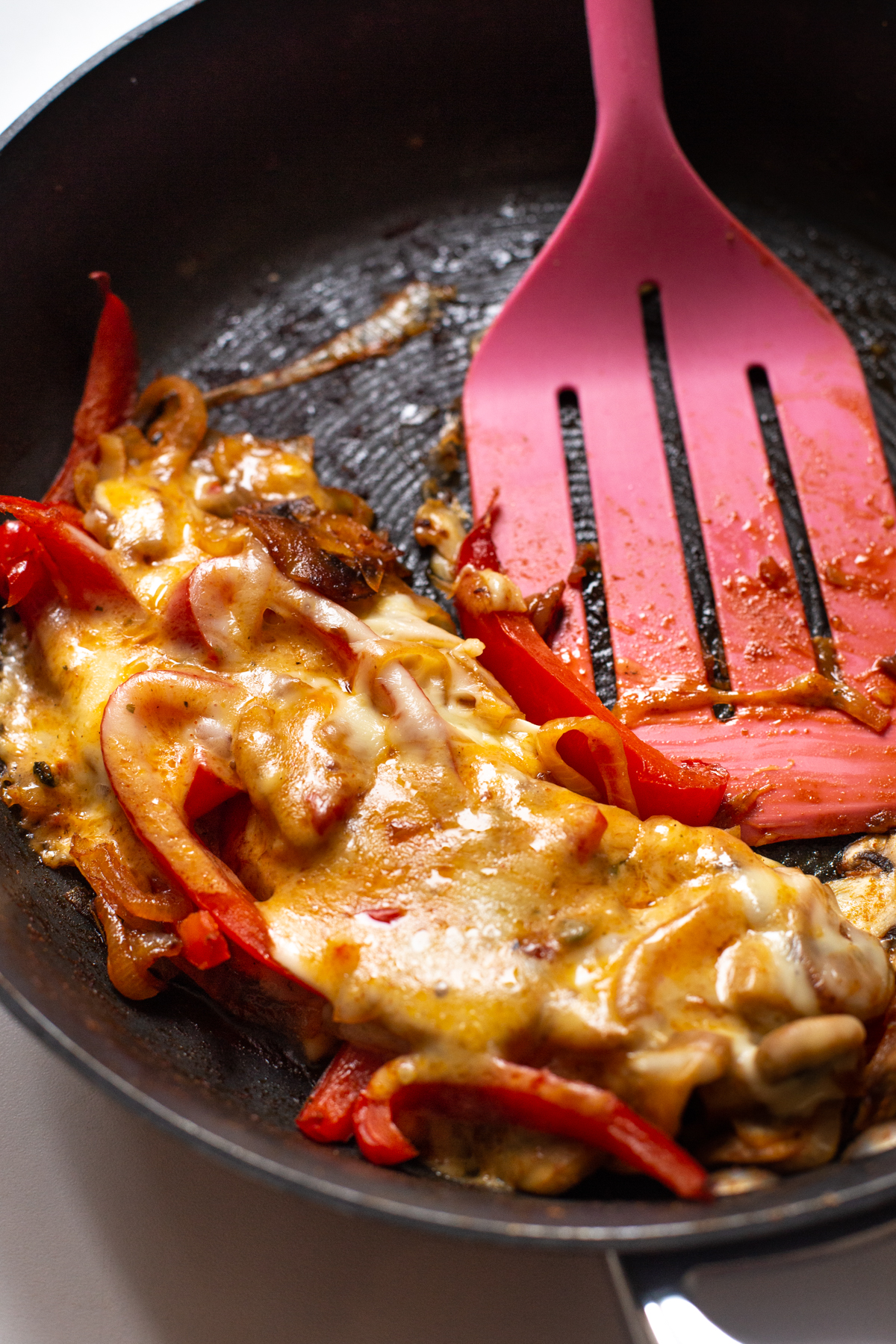 Sautéed vegetables topped with melted cheese in a frying pan.