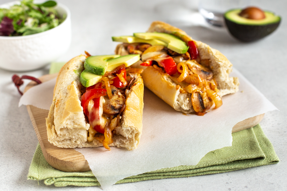 A vegetarian cheesesteak sandwich topped with melted cheese and avocado.