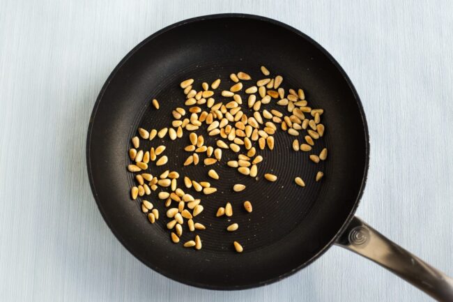 Toasted pine nuts in a frying pan.