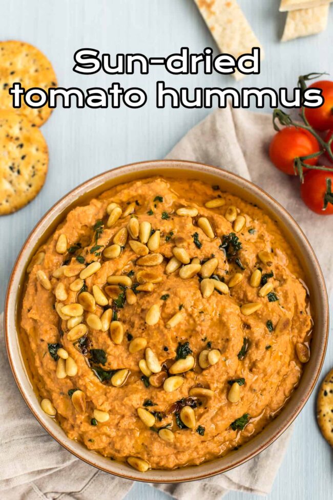 Sun-dried tomato hummus in a bowl topped with toasted pine nuts.